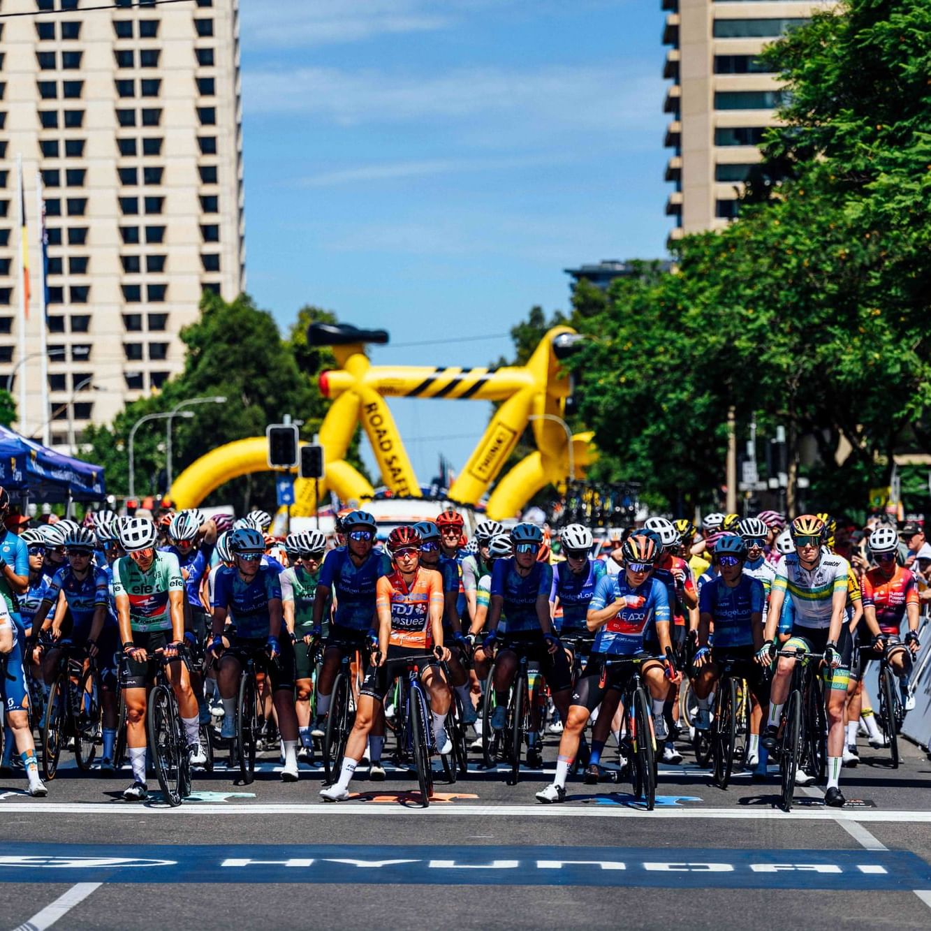 Cyclists gather for the Santos Tour Down Under race on a city street.