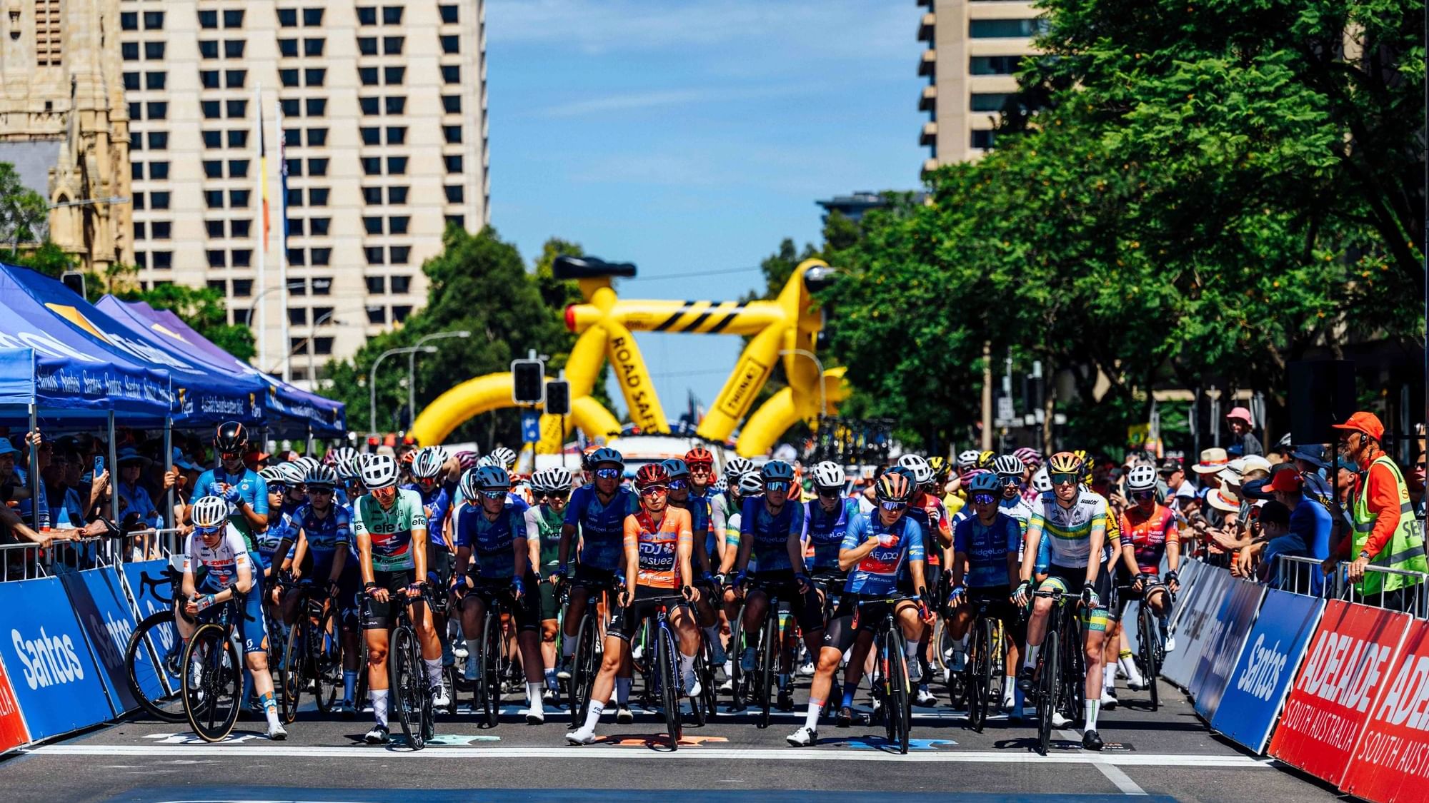 Cyclists gather for the Santos Tour Down Under race on a city street.