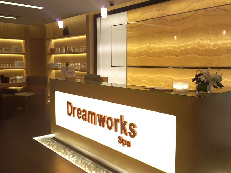 Modern spa reception desk with backlit wall and product shelves in DreamWorks Spa at DAMAC Hotels & Resorts