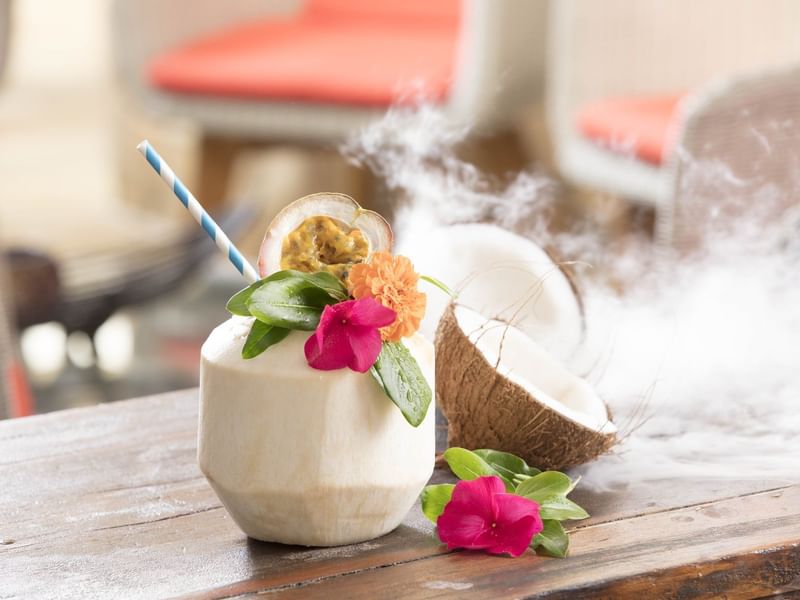 Exotic drink in a coconut with flowers, smoke & a straw on a table in Pool bar at Pullman Port Douglas