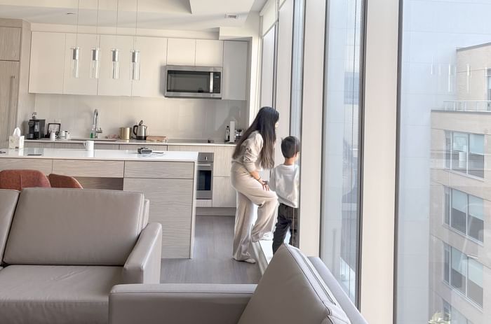 A woman and a child gaze out the large windows of a modern kitchen, surrounded by furniture at ReStays Ottawa