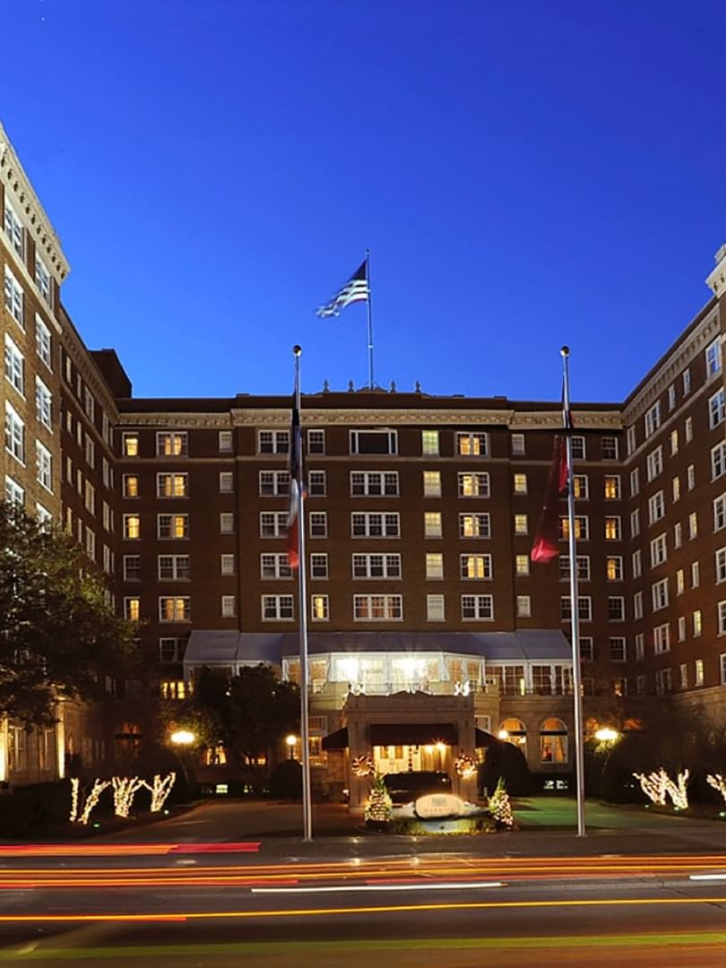 Exterior view of the entrance by lit trees under a twilight sky at Warwick Melrose Dallas