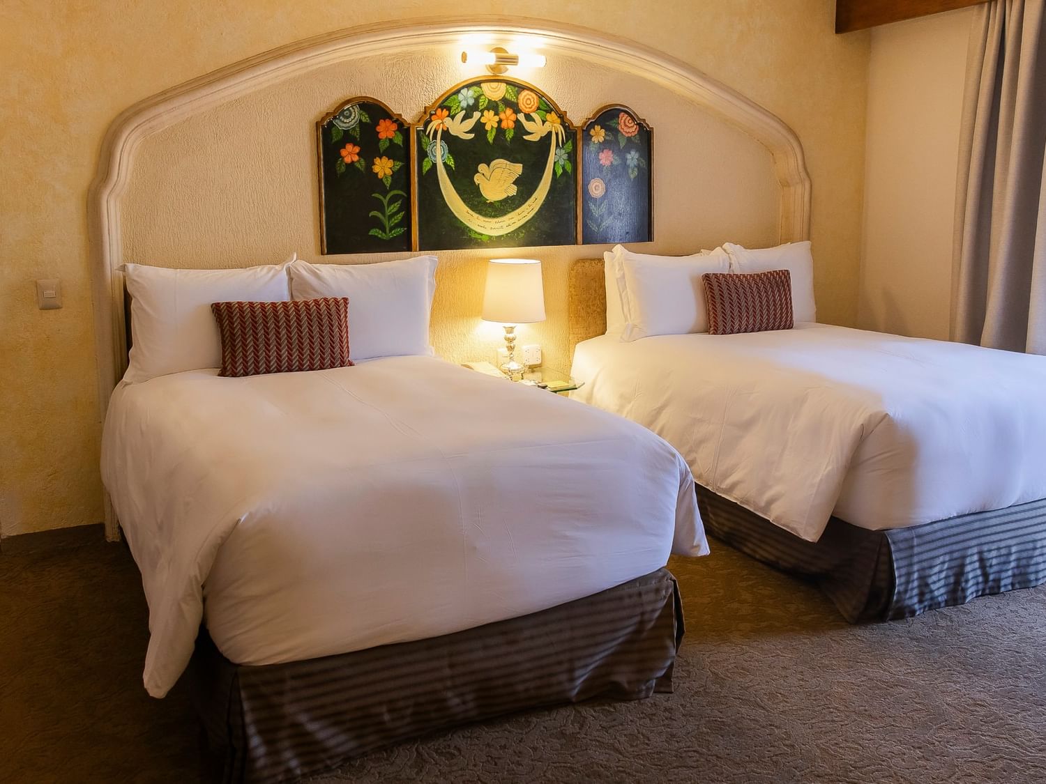 Two double beds with white linens and decorative headboard featuring floral artwork at Quinta Real Zacatecas