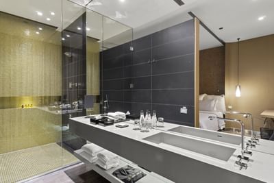 Baño moderno con doble lavabo, espejo grande, cabina de ducha de vidrio y azulejos negros y amarillos.