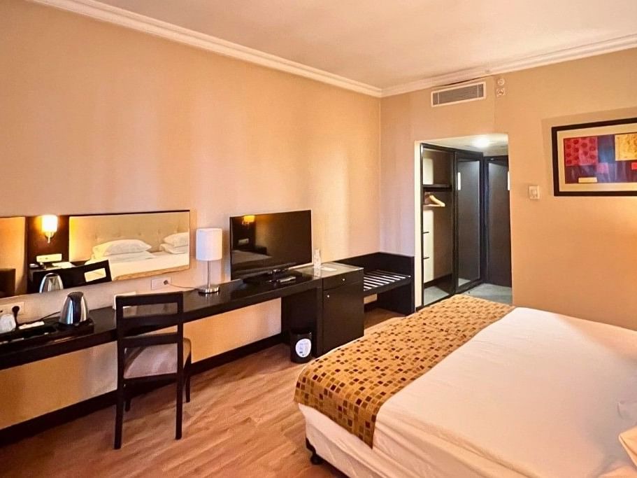 Yatak, sandalye, masa, TV, ayna ve resim içeren otel odası.