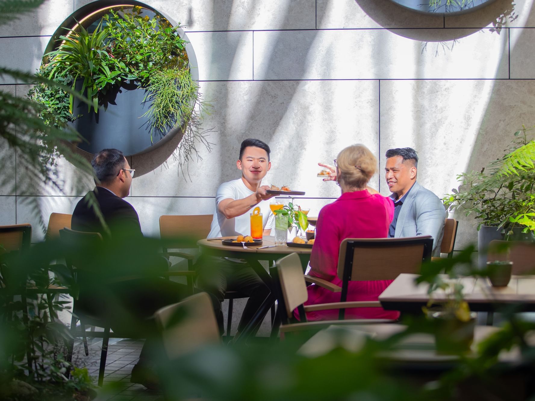 Group of four people seated at a table in an outdoor restaurant surrounded by plants.