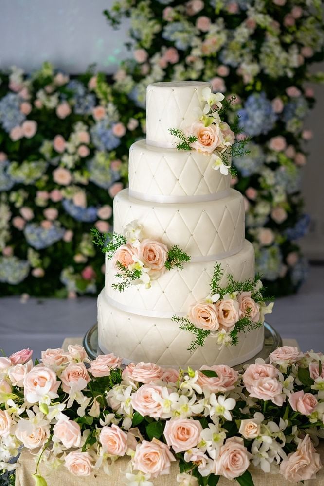 Wedding cake adorned with pink roses and greenery, surrounded by a floral display of roses and orchids at Park Hyatt Saigon