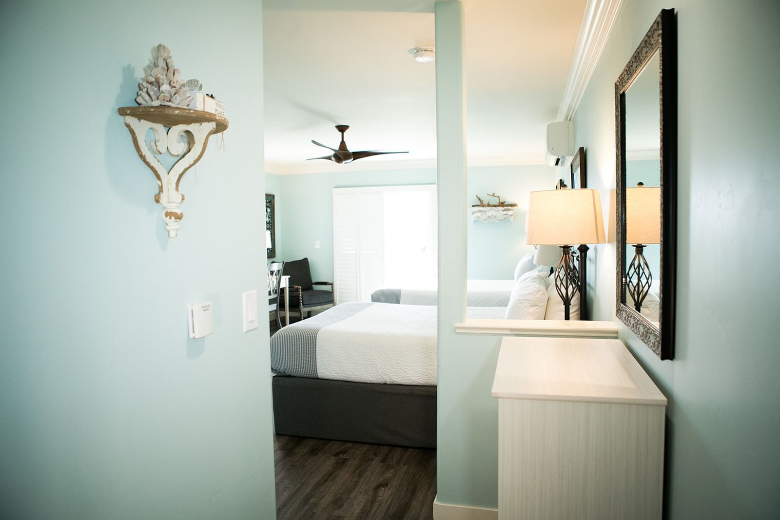 A wide view of a hotel room with a bed, dresser, and shelf.