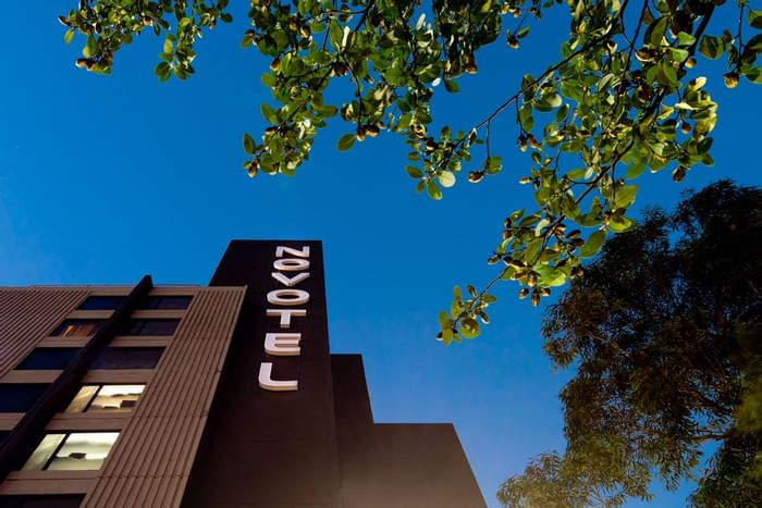 Novotel Sydney International Airport sign under a clear blue sky with green trees in the background