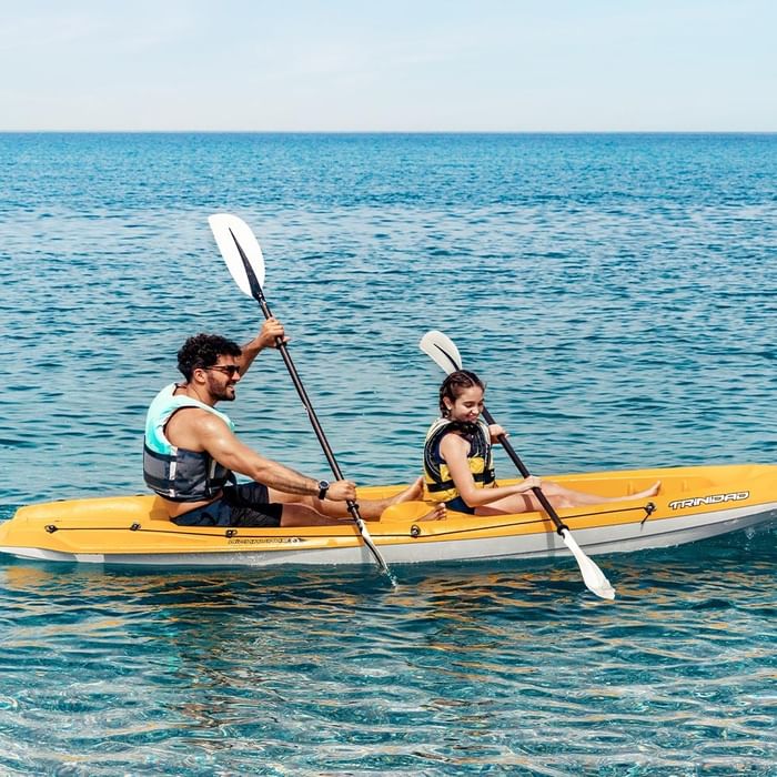 Mann und Kind in gelbem Kajak auf dem Meer, beide mit Paddeln und Schwimmwesten.
