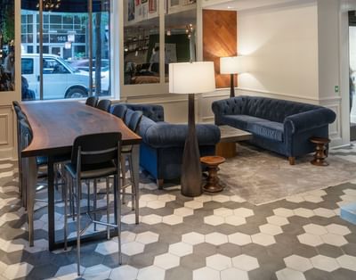 Lobby with blue sofas beside a long wood table under framed Chicago artwork and pendant lights at Hotel Saint Clair