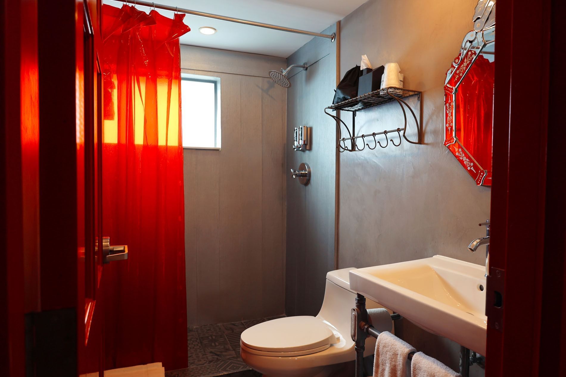 A bathroom with a red shower curtain, a white toilet, and a sink with a mirror above it.