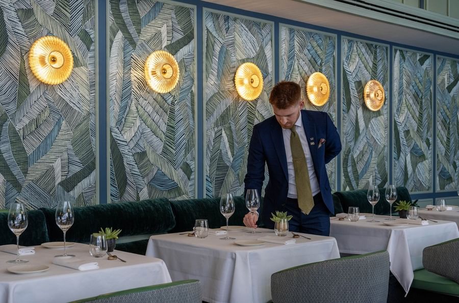 Staff member setting a table with wine glasses & plates at The Capital Hotel, Apartments and Townhouse