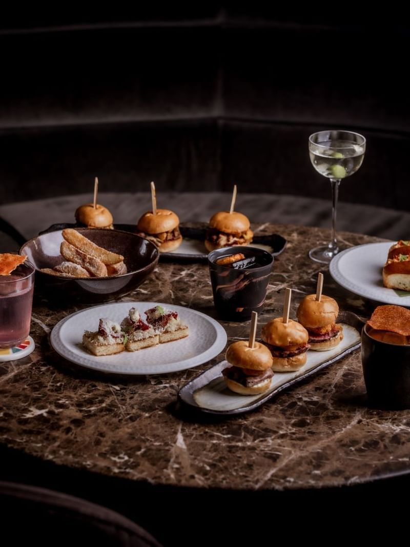 Assorted appetisers and cocktails from the by night menu on a round marble table at The May Fair Bar