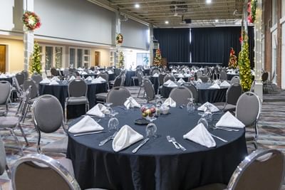 Large ballroom event setup with round tables, black tablecloths, lit Christmas trees, and wreaths at Rodd Royalty