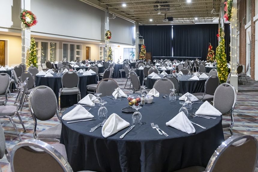 Large ballroom event setup with round tables, black tablecloths, lit Christmas trees, and wreaths at Rodd Royalty