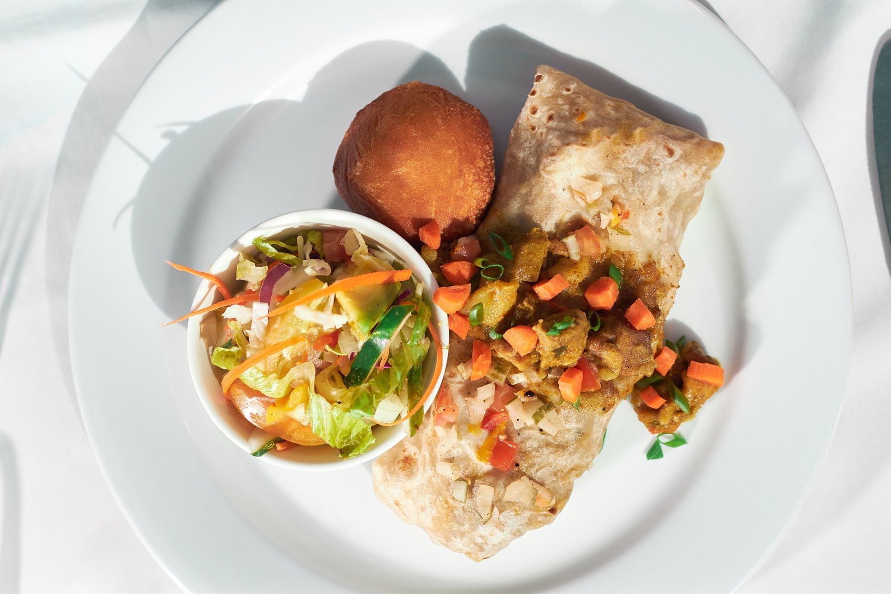 Plate featuring a spiced burrito topped with diced vegetables, a side of colorful salad, served at Bay Gardens Marina Haven
