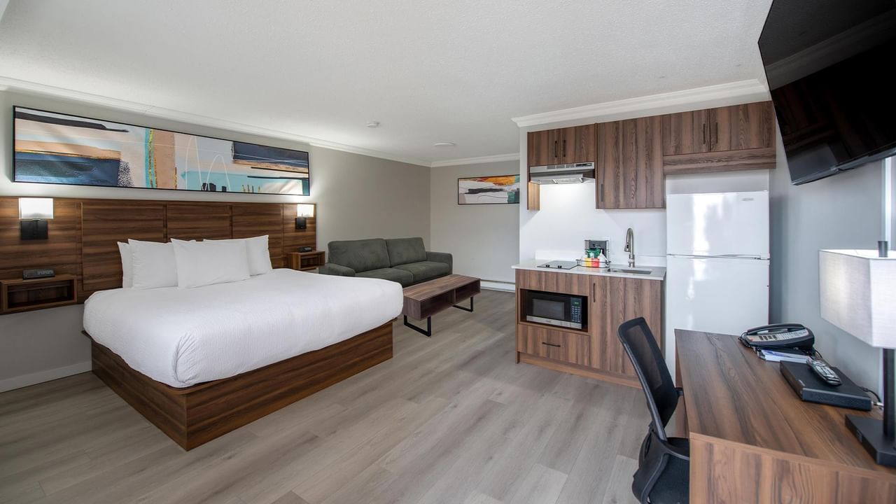 Hotel guest room with a king bed, sofa, kitchenette, work desk and wall-mounted flat-screen TV.