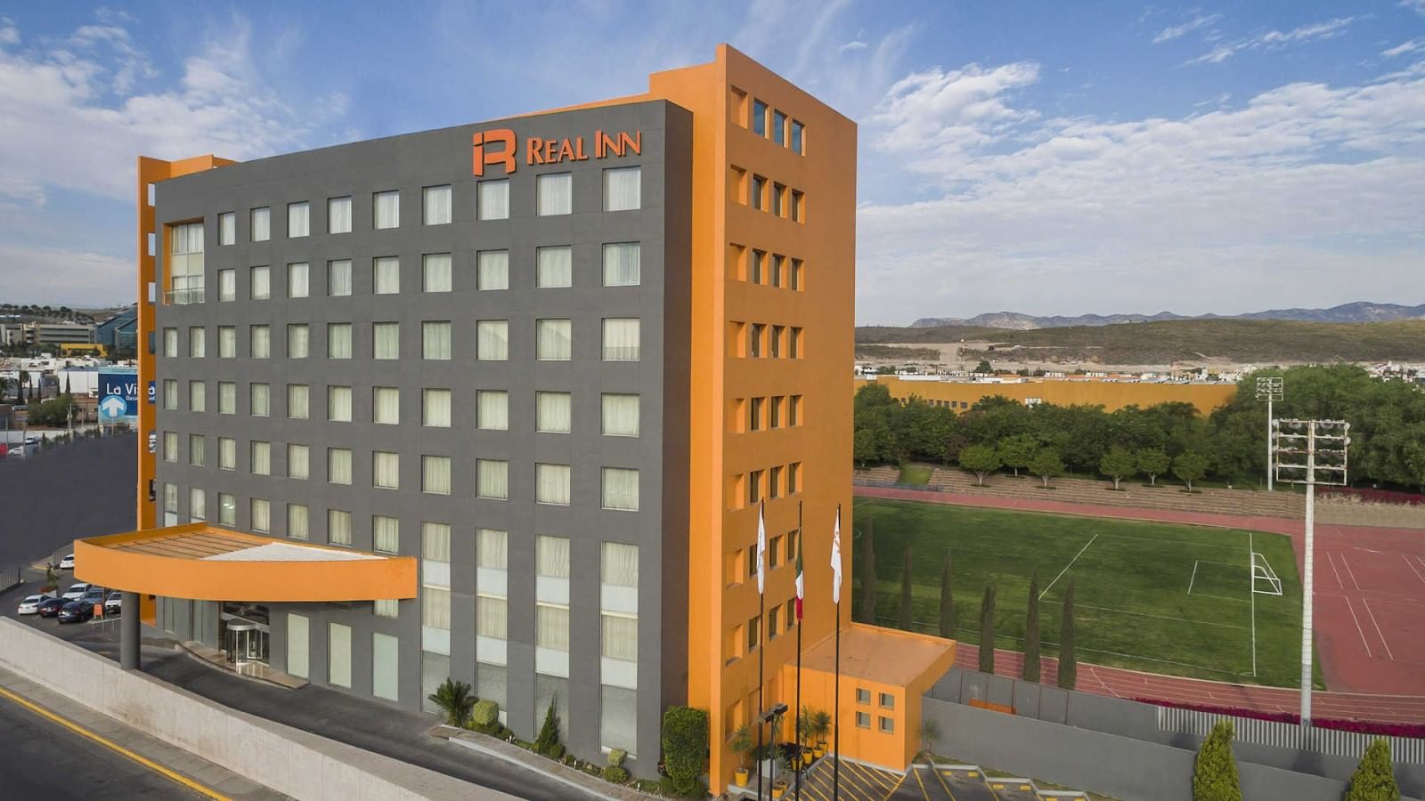 Orange and gray facade of Real Inn San Luis Potosi with a parking lot and city views