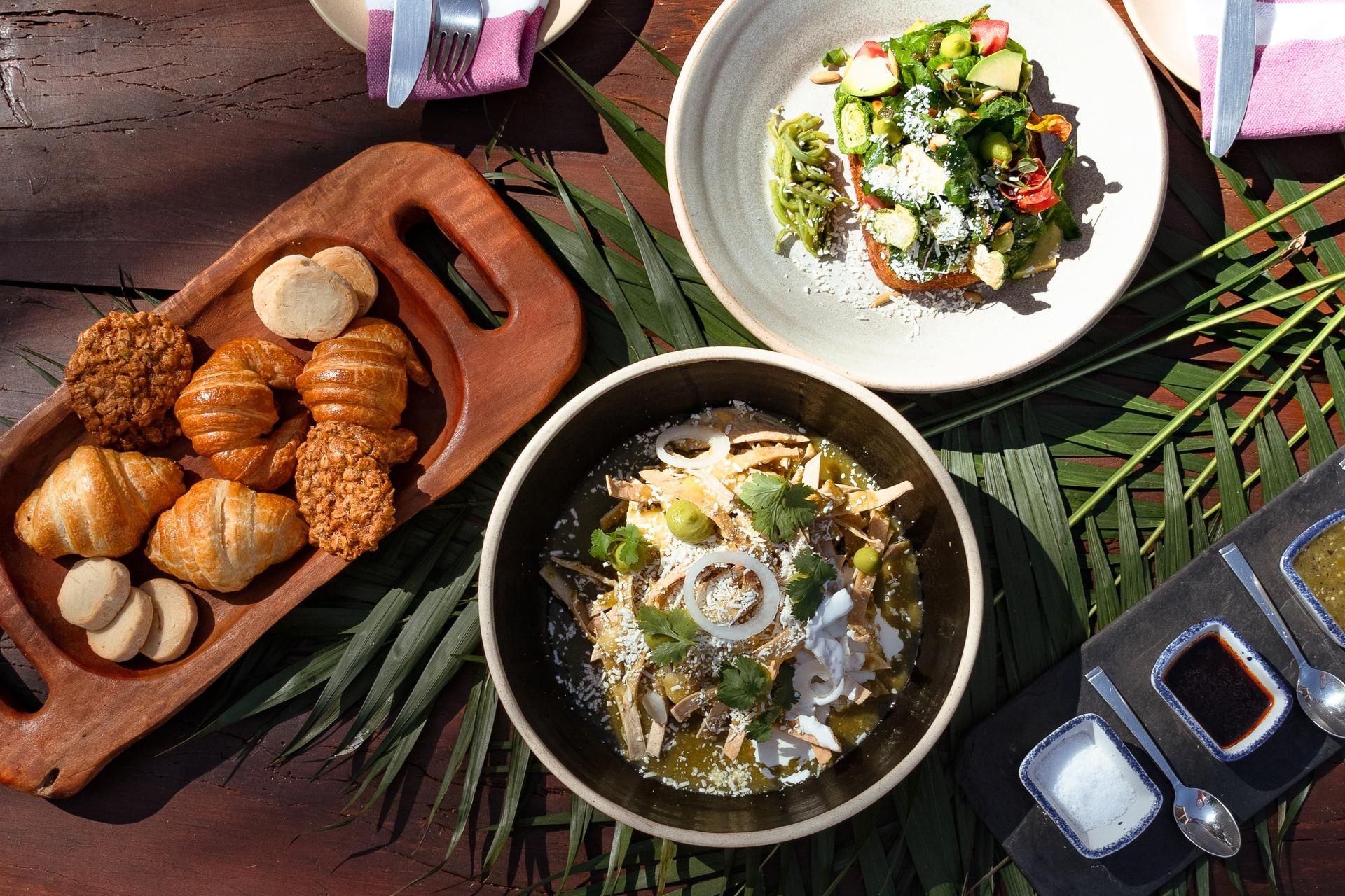 An overhead view of a sunny breakfast with Mexican dishes like chilaquiles salad and pastries at La Zebra Hotel