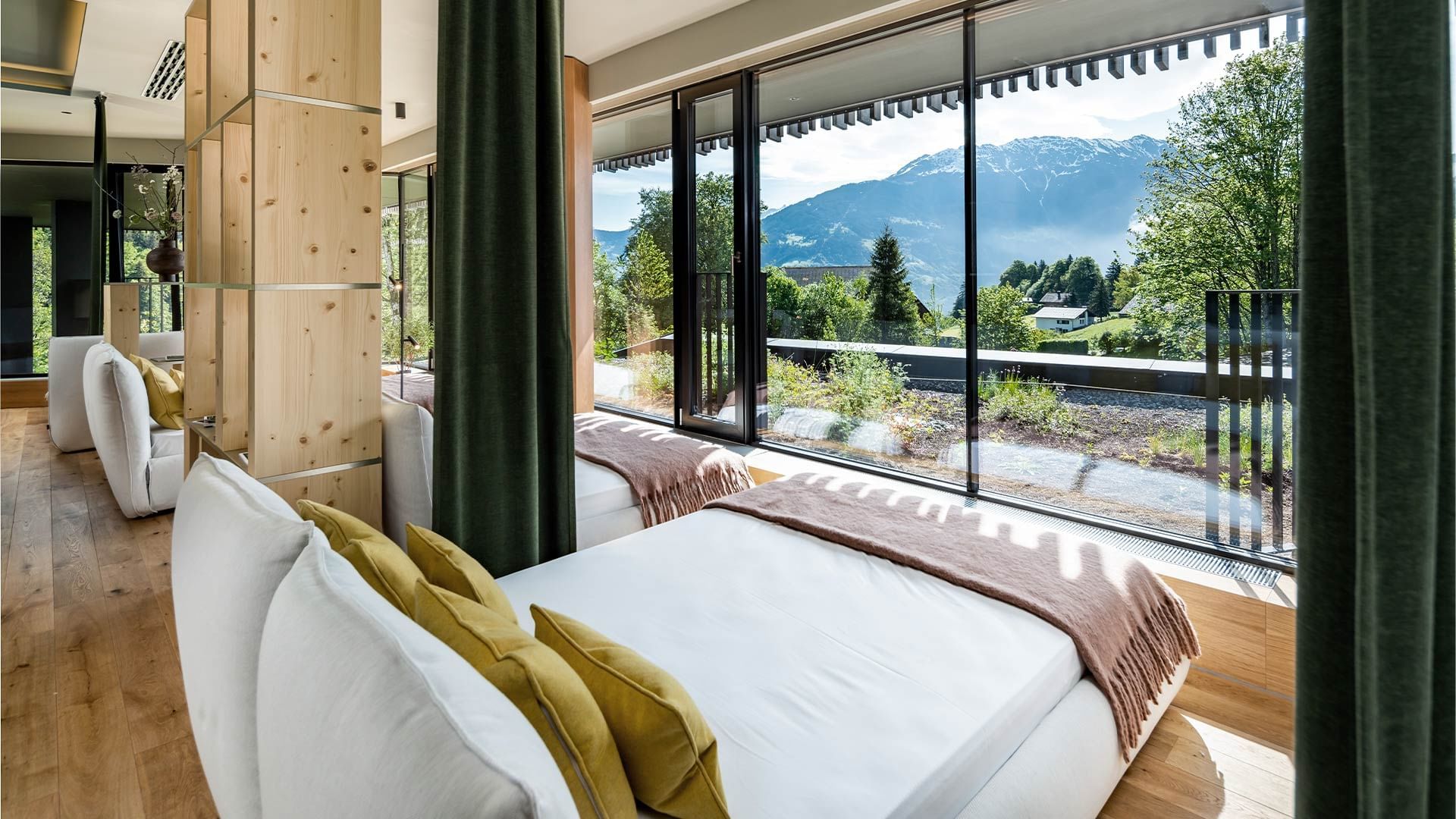 Zimmer mit weißen Betten, Holzboden und Panoramablick auf Berge und Wald.