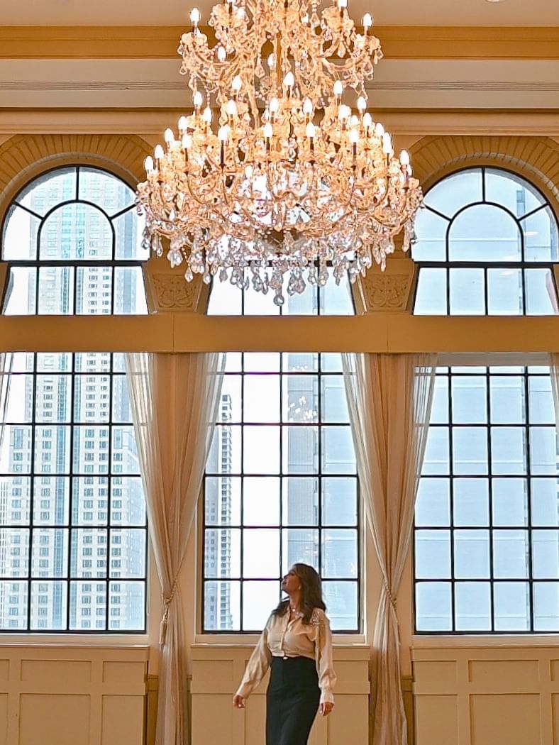 Salle de réception élégante avec lustre en cristal et hautes fenêtres cintrées offrant une vue urbaine panoramique