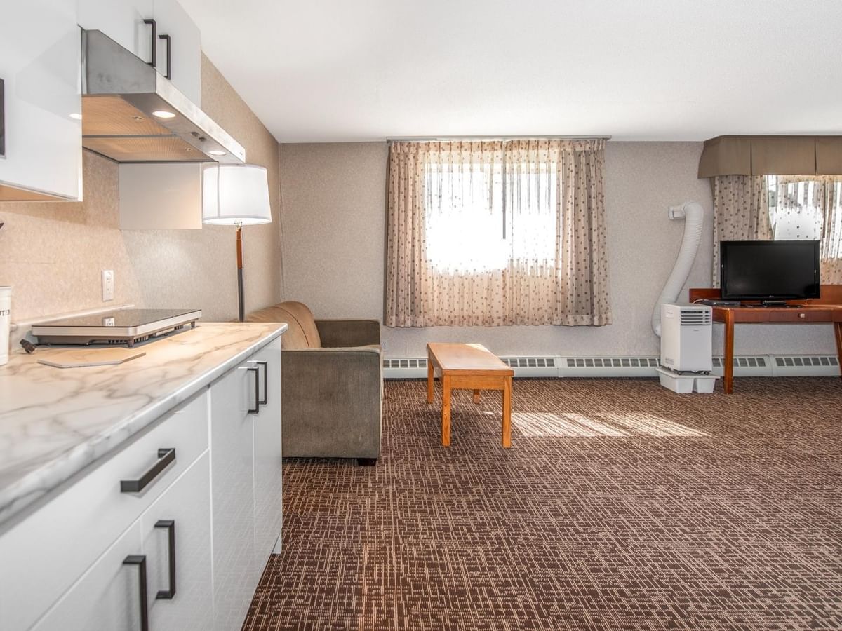 Living area with couch, coffee table, TV, and kitchenette with white cabinets and countertop.