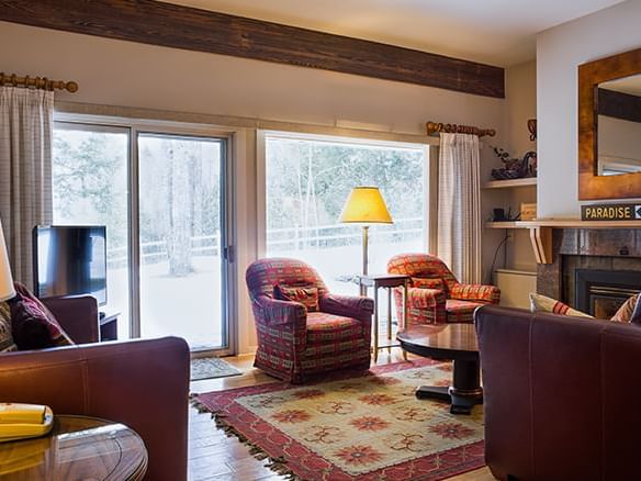 Cozy living room with exposed beams, patterned armchairs, and snowy forest views at Topnotch Stowe Resort in Stowe