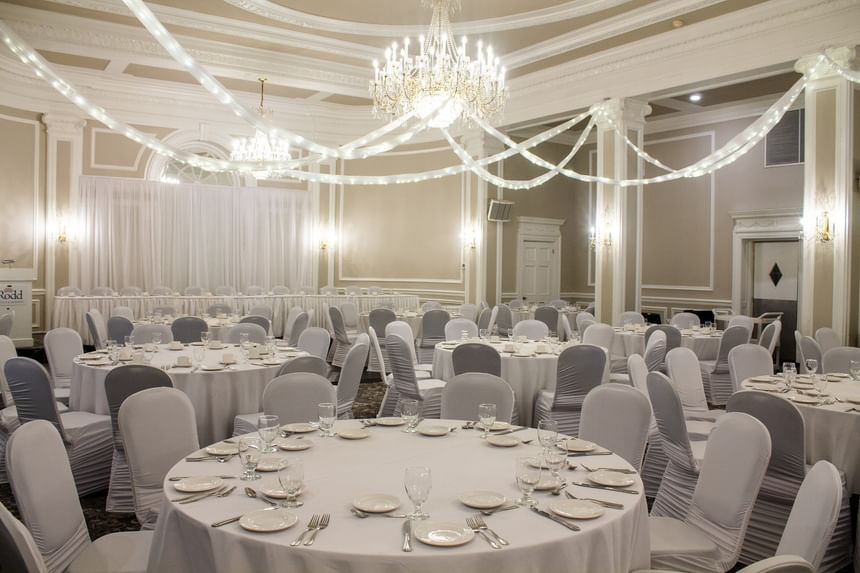 Round dining tables with white cloths under hanging decorative lights in a ballroom at Rodd Charlottetown Hotel