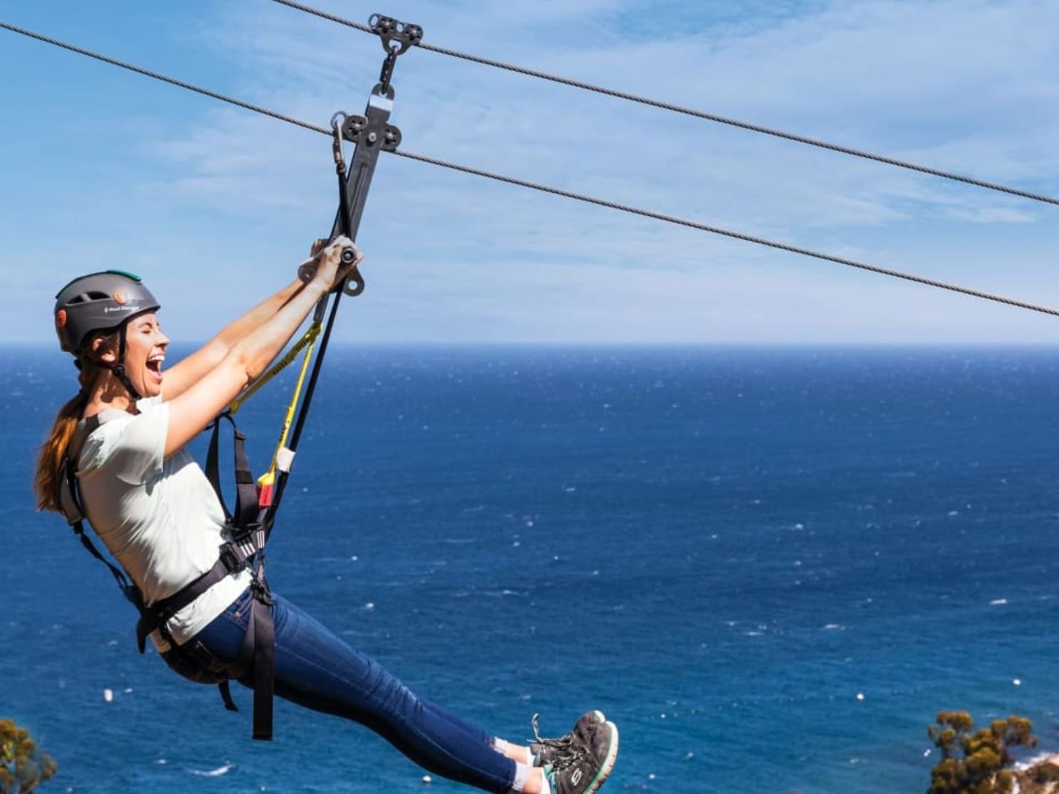 A woman zip-lining over a blue ocean with clear sky near Catalina Island Company