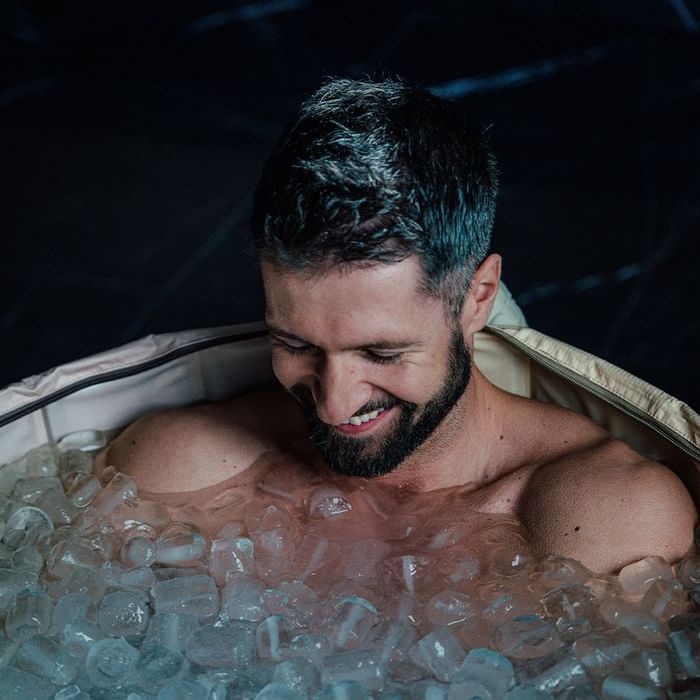 Uomo con barba e capelli grigio-neri in una vasca piena di ghiaccio, sorridente.