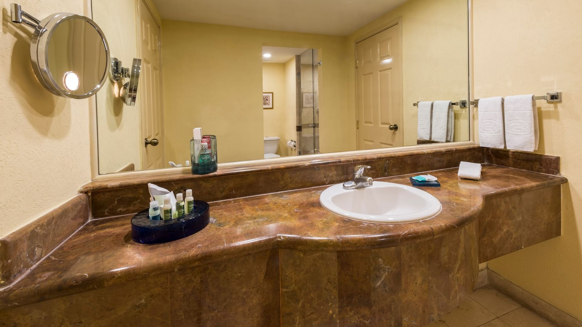Baño con cubierta de mármol, lavabo ovalado, espejo amplio y amenidades en Camino Real Puebla Angelópolis