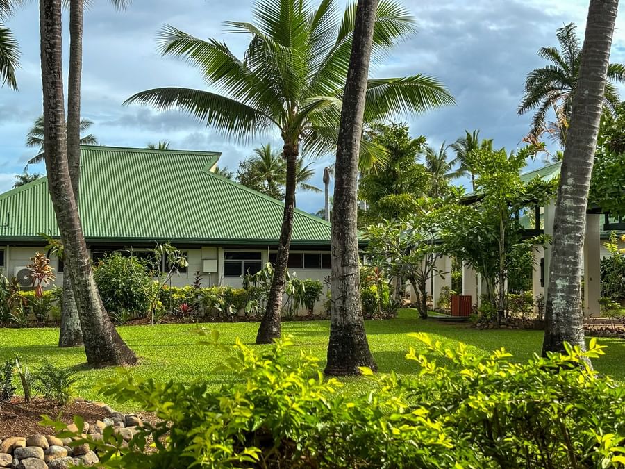Green-roofed resort buildings by a grassy lawn surrounding tall palm trees at TokaToka Resort Nadi Fiji