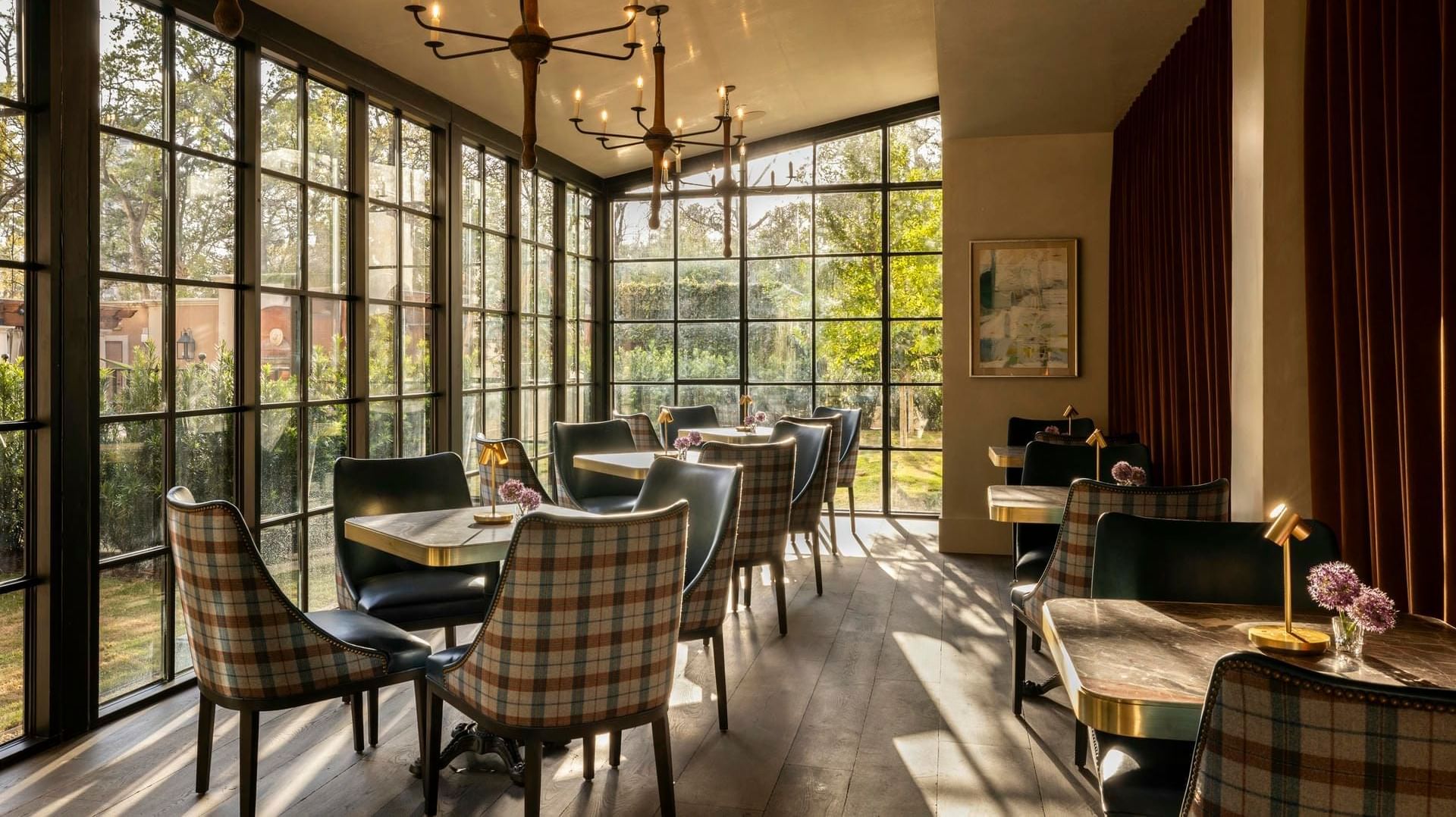 Elegant interior of The Primrose Room at Granduca Houston with plaid chairs and scenic views of lush greenery outside