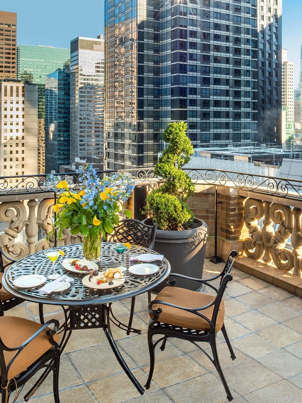 Round dining table with floral centerpiece placed by chairs on a balcony terrace in 54th Suite Terrace at Warwick New York