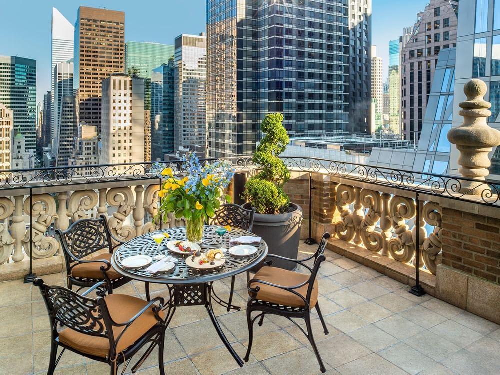 Round dining table with floral centerpiece placed by chairs on a balcony terrace in 54th Suite Terrace at Warwick New York