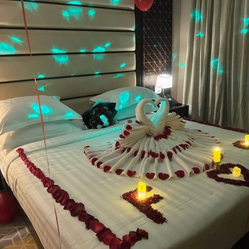 Room at Warwick Hotels and Resorts, decorated for a romantic evening with rose petals, candles, and a towel swan on the bed