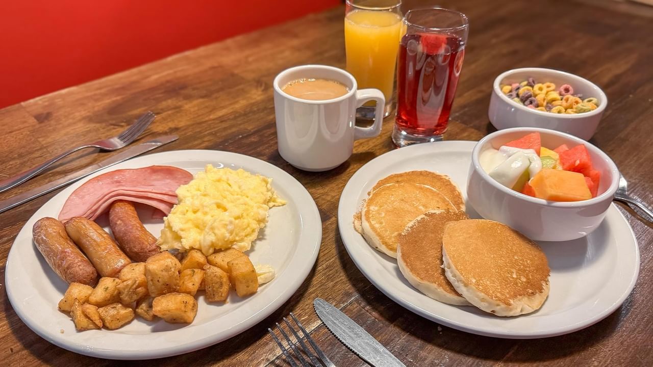 Plates of breakfast food with fruit salad, ham, eggs, coffee, and juice.