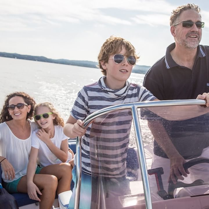 Familie genießt den Tag auf einem Boot, mit einem Mann am Steuer und drei Passagieren.