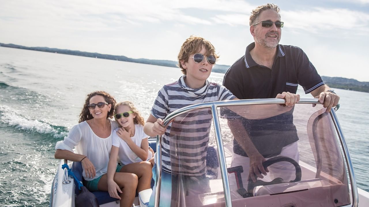 A family of four, all wearing sunglasses, enjoys a day out on a pink motorboat.