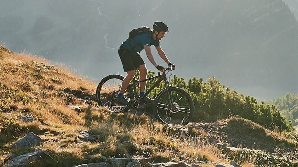 Cyclist riding on a rugged trail with a mountain backdrop near Falkensteiner Hotel Schladming