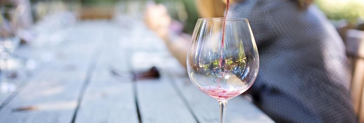 Person pouring a glass of red wine on a light-colored wooden table at The Sebel Mandurah