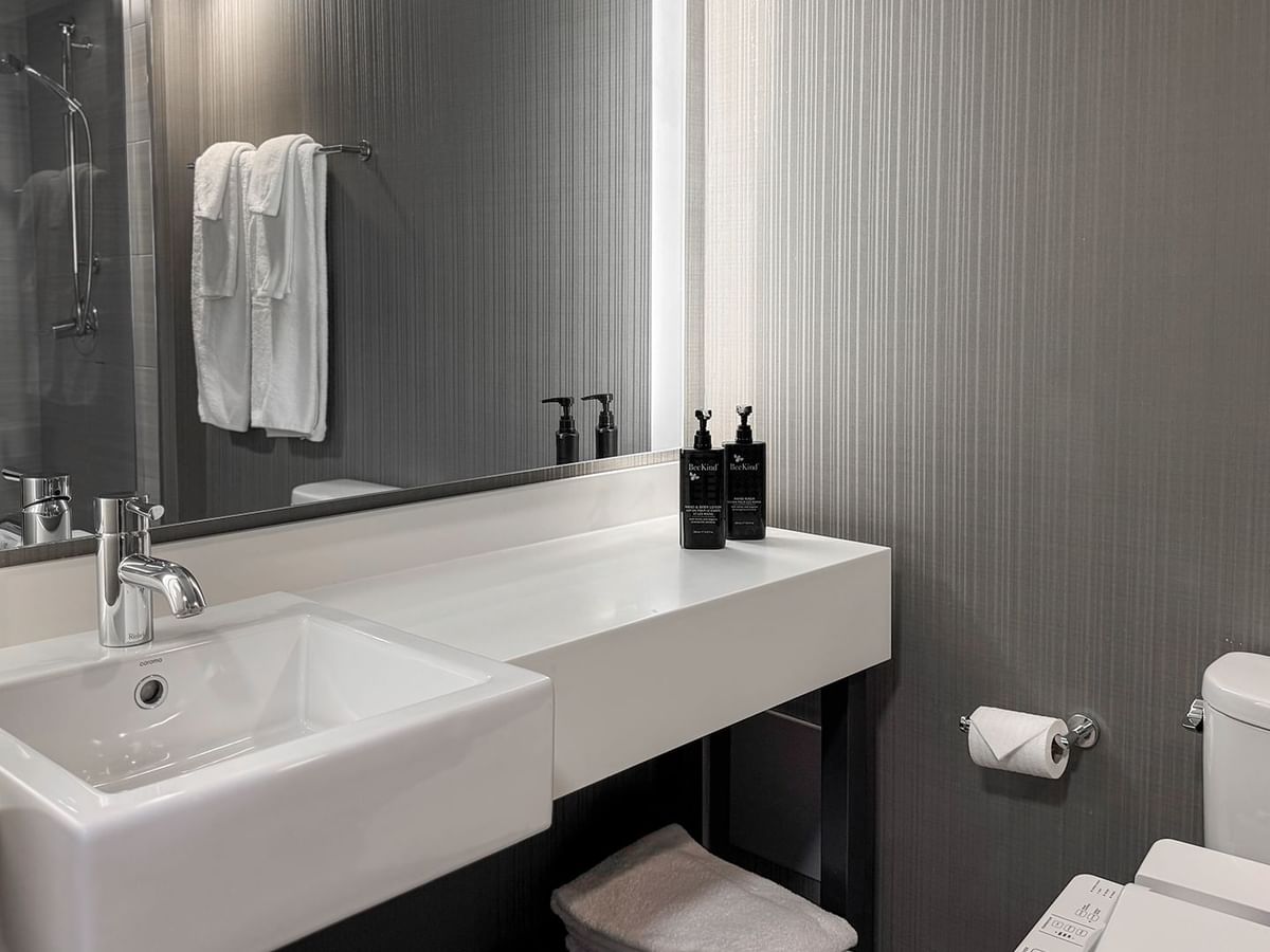 Modern bathroom with white sink, gray walls, toiletries, and toilet.