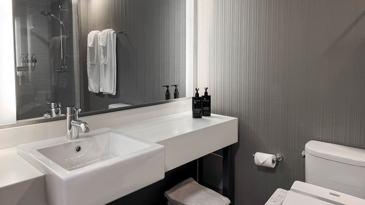 Modern bathroom with white sink, gray walls, toiletries, and toilet.