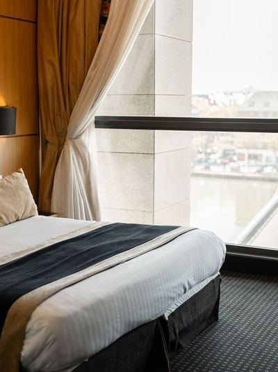 Chambre d'hôtel élégante avec lit, bureau et vue sur le bassin du commerce par une grande fenêtre.