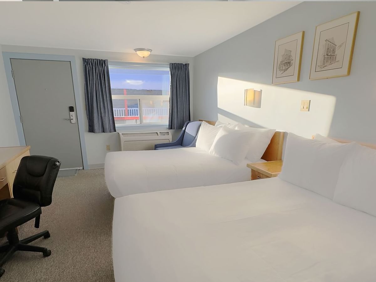 Two double beds, a work desk and a chair in front of a window