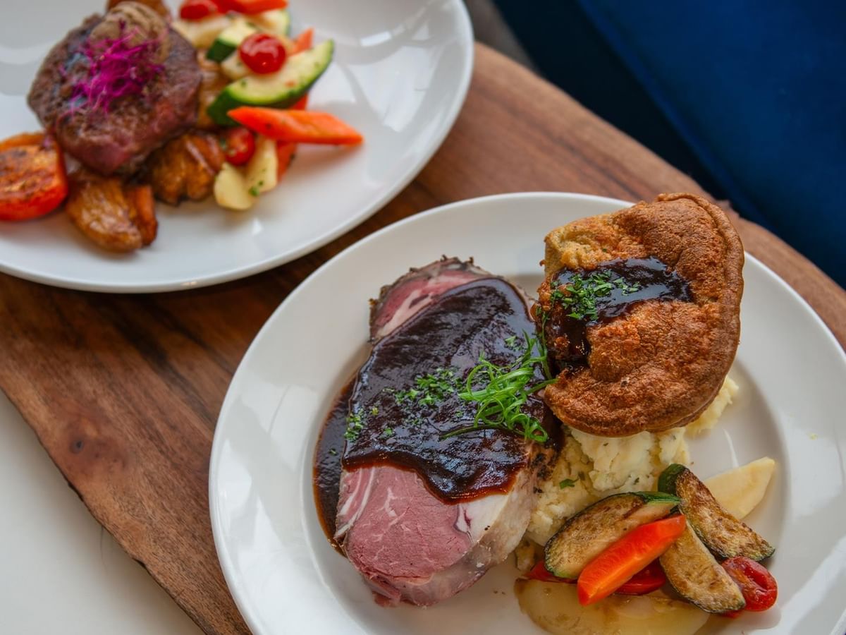 Two plates with beef, vegetables, and sauces at Minnoz Restaurant + Lounge in Nanaimo at Coast Bastion Hotel.