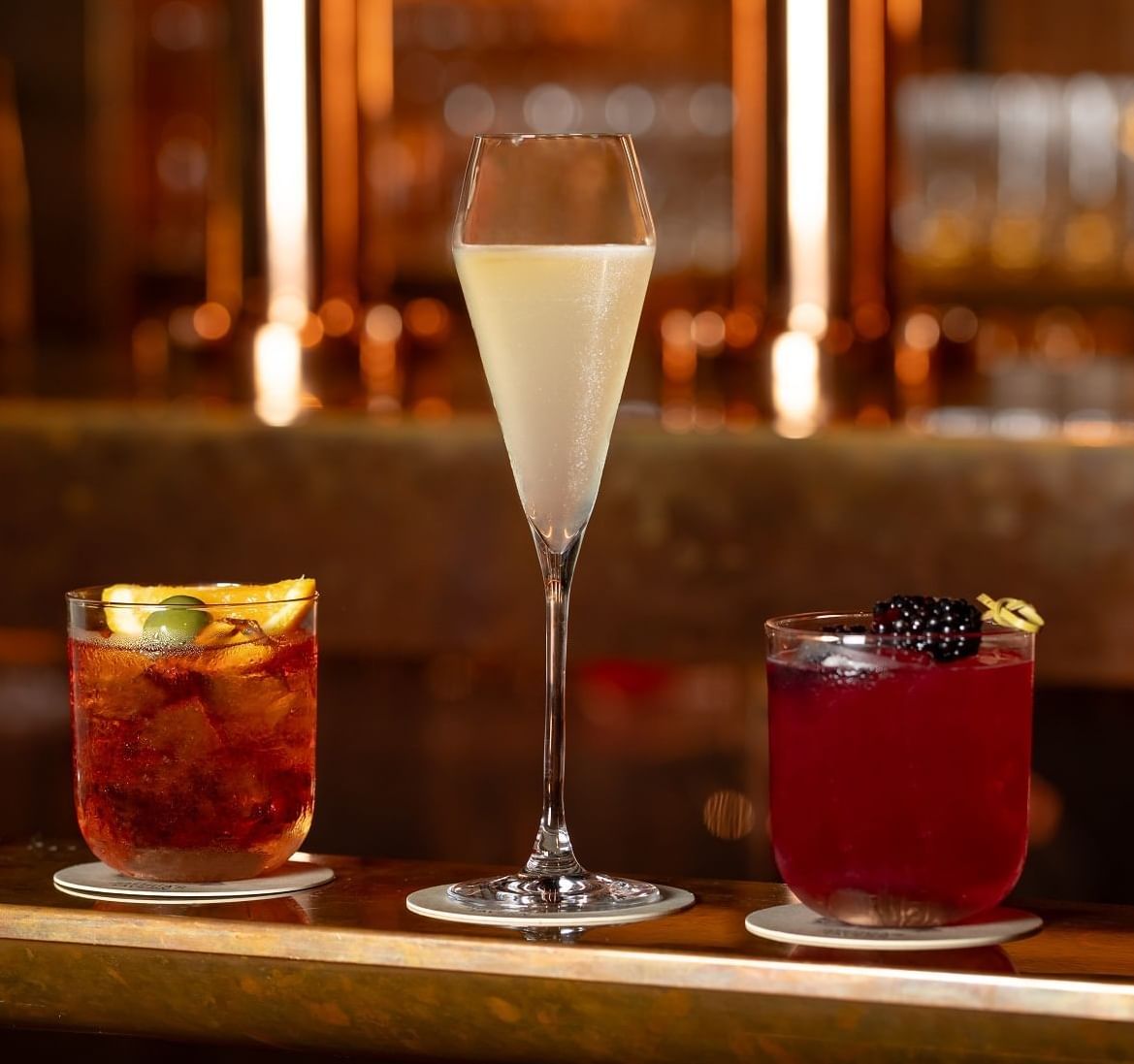 Four vibrant Negroni and Tom Collins cocktails lined up on the bar at Joshua’s Tavern in The Londoner