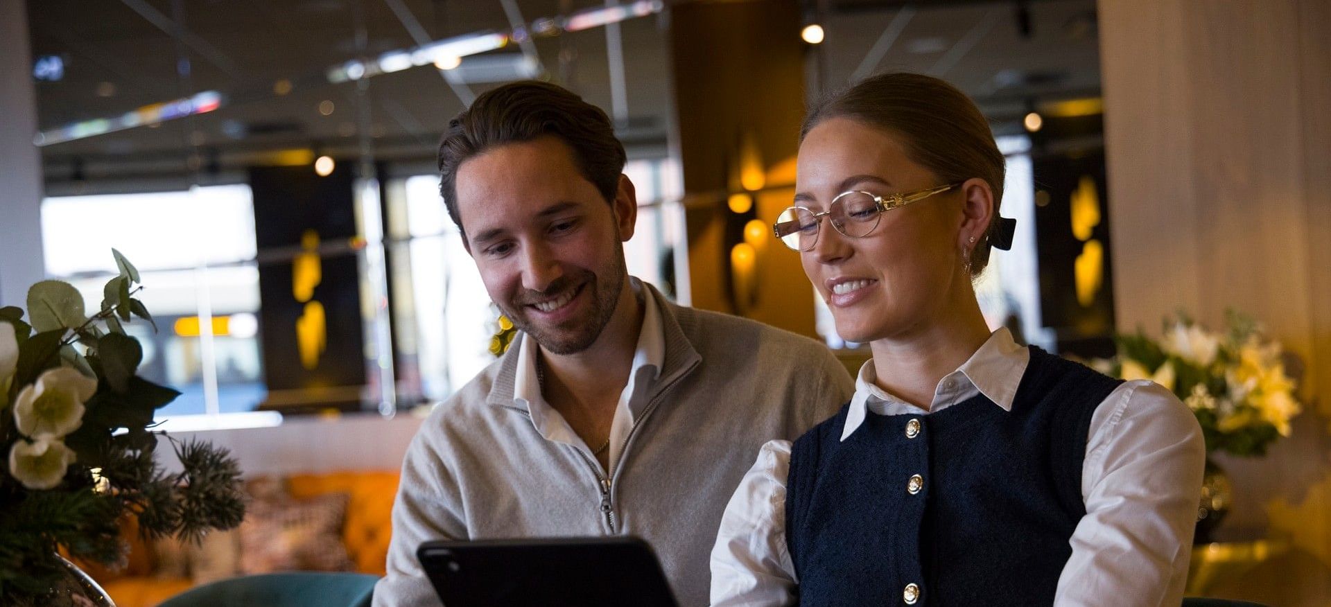 Två gäster sitter i The Livingroom på Hotel Riverton och arbetar tillsammans vid ett bord.
