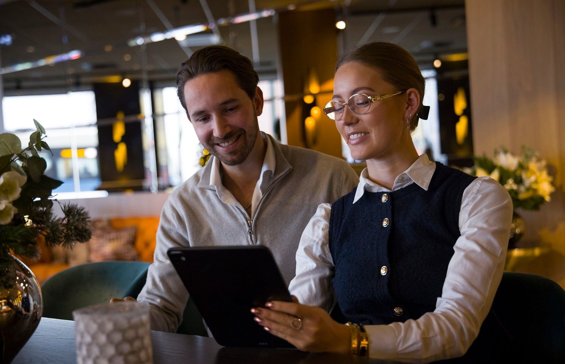 Två gäster sitter i The Livingroom på Hotel Riverton och arbetar tillsammans vid ett bord.